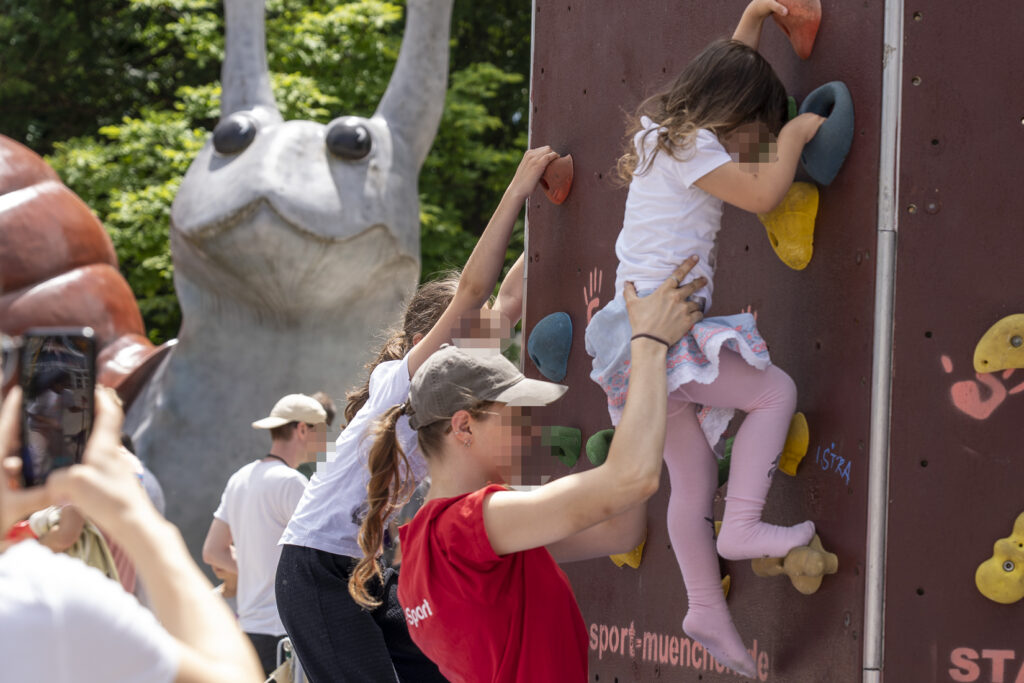 Im Vorderdrund eine Boulderwand, an der zwei Kinder klettern. Im Intergrund der Kopf einer großen Schnecke.