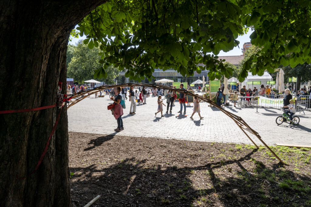 Eine selbstgebaute Holzbrücke im Vordergrund, dahinter der Platz